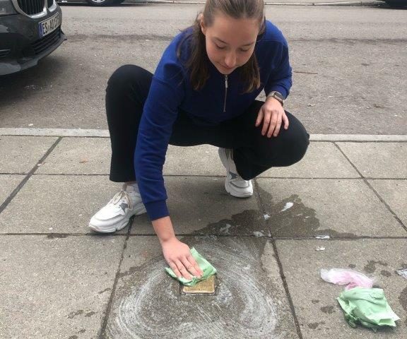 Schülerinn reinigt Stolperstein