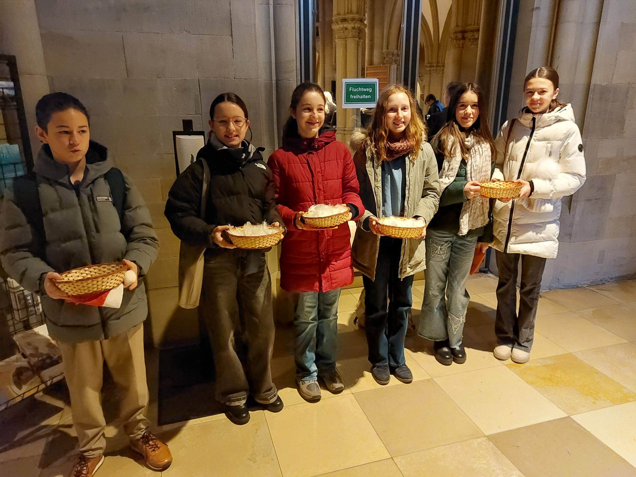 6 Kinder stehen vor dem Eingang einer Kirche und teilen Federn aus.