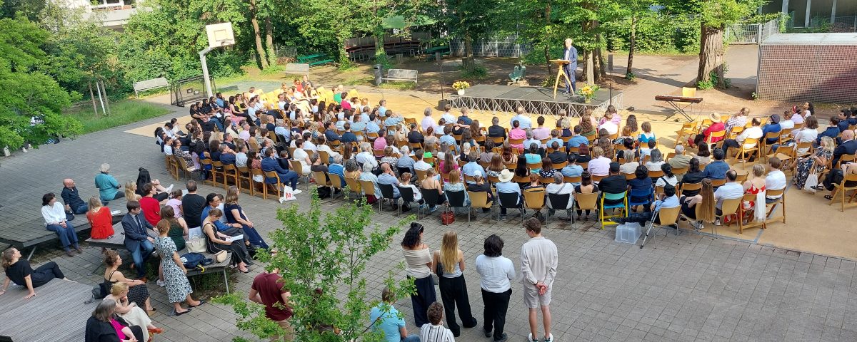 Blick von oben auf Schulhof auf welchem Abi ausgabe stadfindet, Herr Wolnitz spricht auf Schulhof