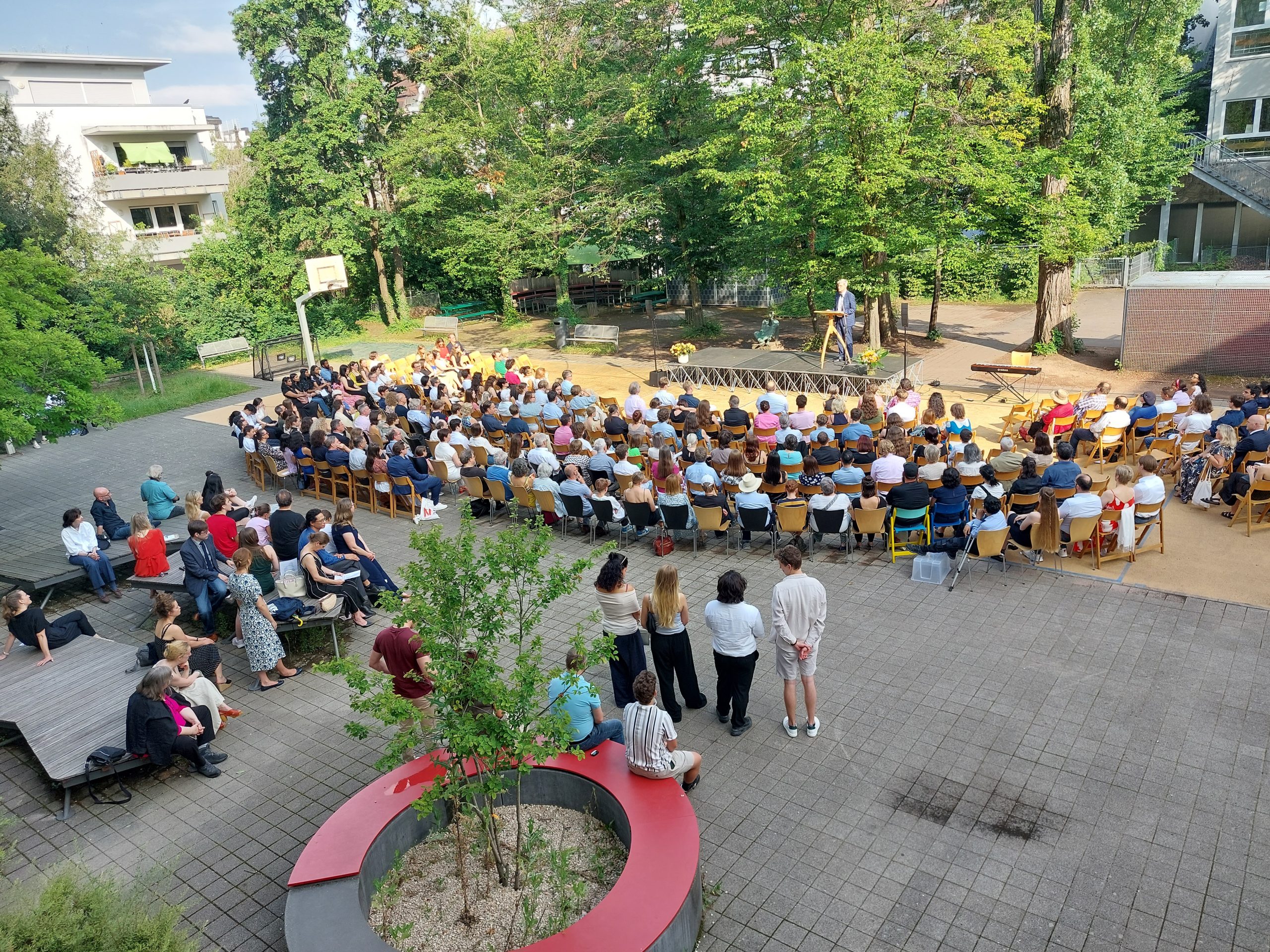 Abi 24 1; Vorschau Blick von oben auf Schulhof auf welchem Abi ausgabe stadfindet, Herr Wolnitz spricht auf Schulhof